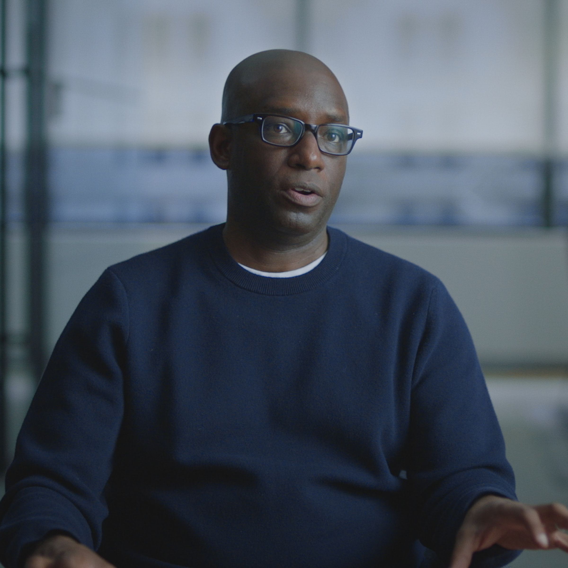 A bald man wearing glasses and a blue sweater in a boardroom.