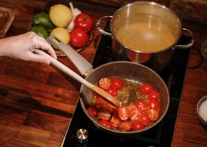 sautéing tomatoes in a pot next to simmering broth