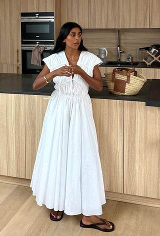 a photo of a woman wearing a white dress outfit with black flip flops and raffia bag