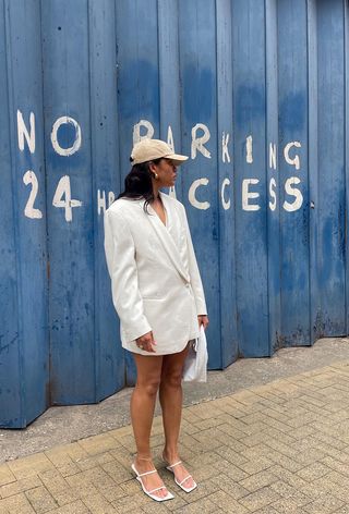 a photo of a woman's white dress outfit styled with a baseball cap and white sandals