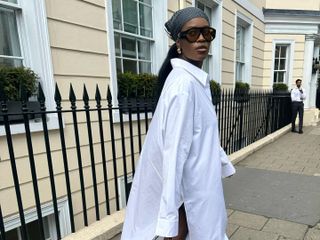 Woman wears a long white shirt dress, Alaia open weave Mary Janes, Chanel purse and hair scarf.