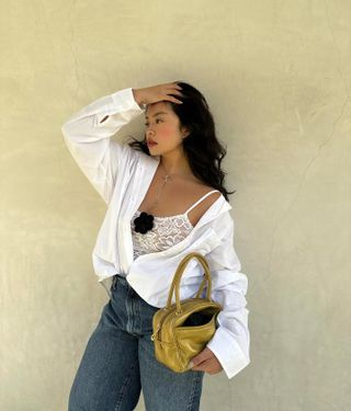 Woman against wall wears lace top with corsage, shirt and jeans