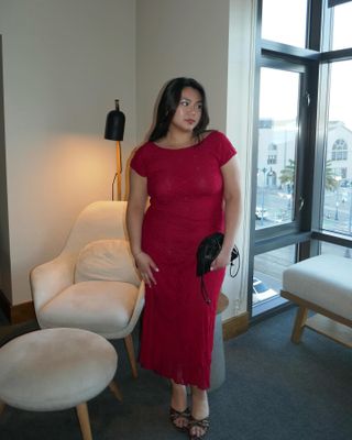 woman wearing red cap sleeve body con dress, leopard peep toe mule shoes, black pouch drawstring bag, in apartment setting