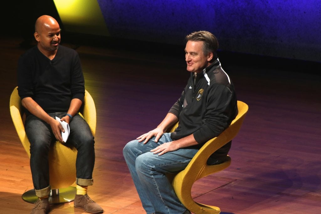 A photo of Kayak co-founder Paul English sitting on a chair on stage speaking at a conference. 