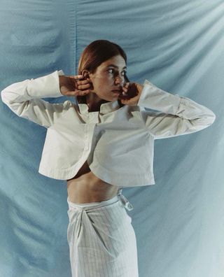 Woman wearing white breezy Liberowe cropped jacket against light-blue background.