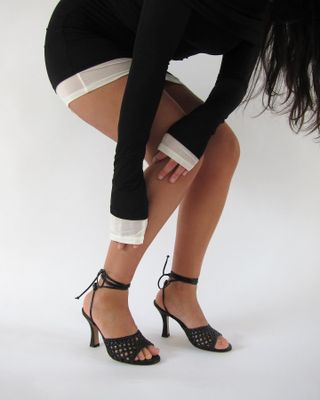 Model reaching down to tie black strappy heeled sandals from Maile.