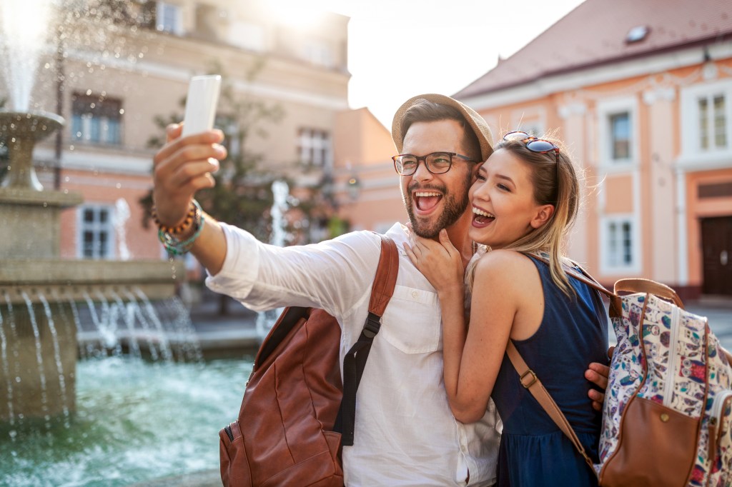 A happy tourist couple in love, laughing and taking a selfie while on vacation