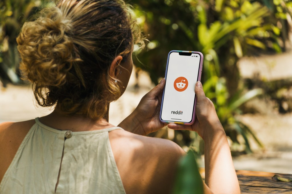 Girl in a park in Rio de Janeiro, Brazil, holding a smartphone displaying the Reddit app on a rustic wooden table