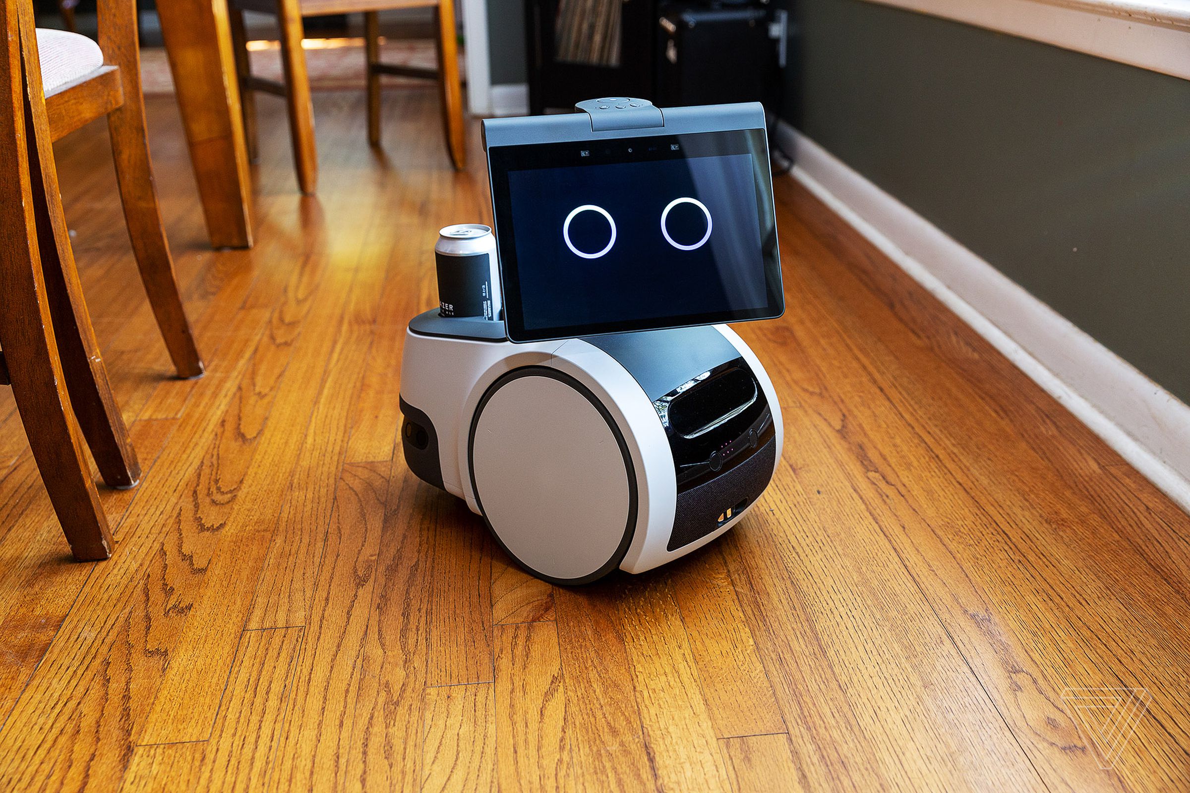 Astro robot with wheels, big circles for eyes, and a can in its trolley, on a wooden floor.