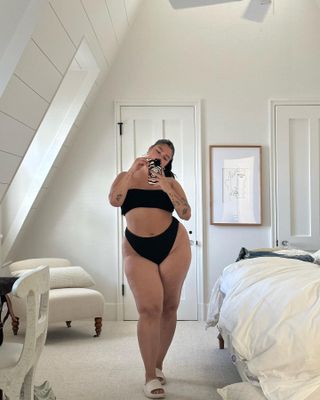 Content creator taking a mirror selfie in a black swimsuit