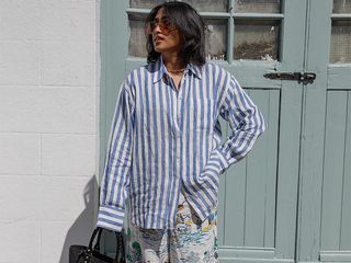 chiara wears white and blue striped button down and loose printed pants while holding a straw tote