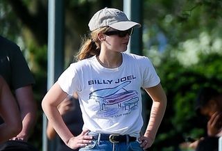 Jennifer Lawrence wearing a hat, white Billy Joel T-shirt, wide-leg jeans, and Vans sneakers.