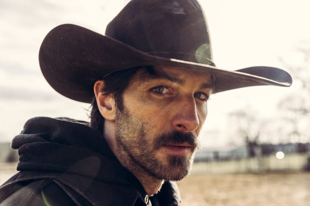 A cowboy with an unshaven face and a worried look on his face.