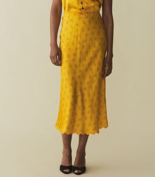 a model wears a yellow satin floral midi skirt