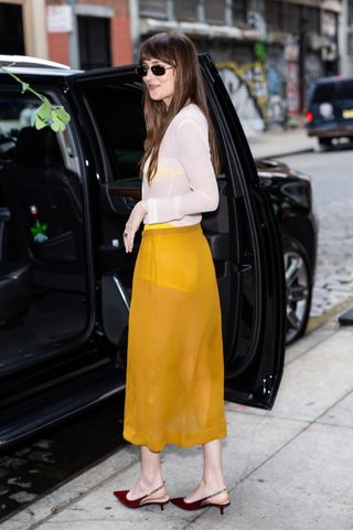 Dakota Johnson wears a yellow midi skirt with burgundy heels