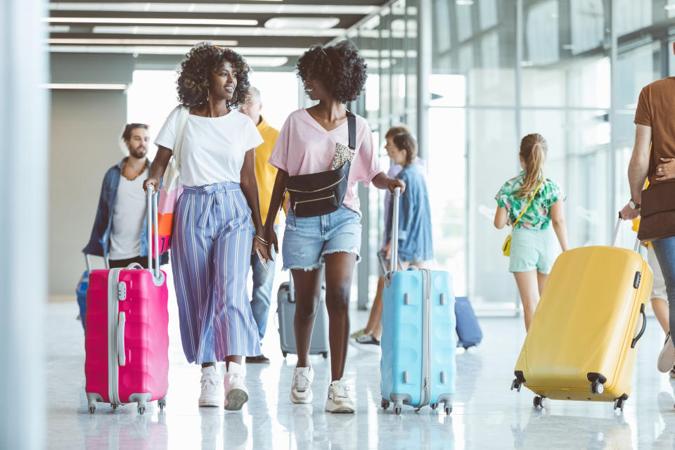 Multiracial passengers walking with wheeled luggage at airport.