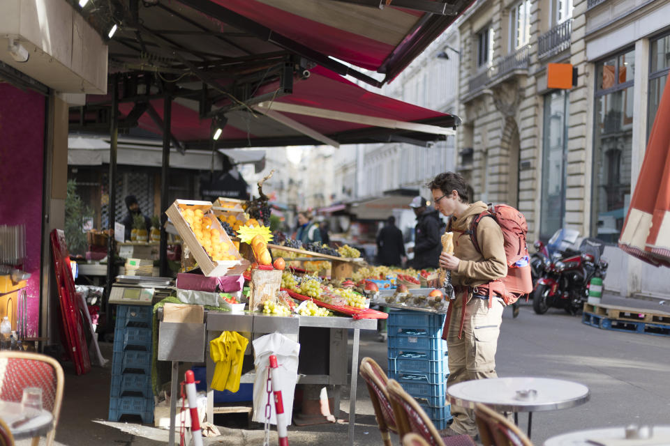 A young man holds a baguette and cheese travels with his backpack through the streets of Paris France and looks at the fresh fruit during the autumn time. stock - photo