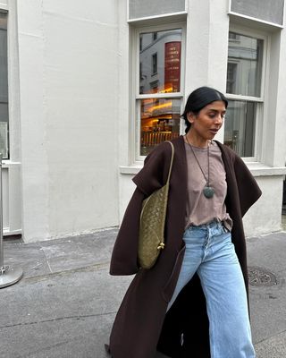 @monikh wearing t-shirt, jeans, brown coat, and a long necklace with a green stone pendant