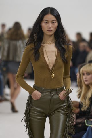 Chloe model wearing knit top, leather pants, and long gold necklace