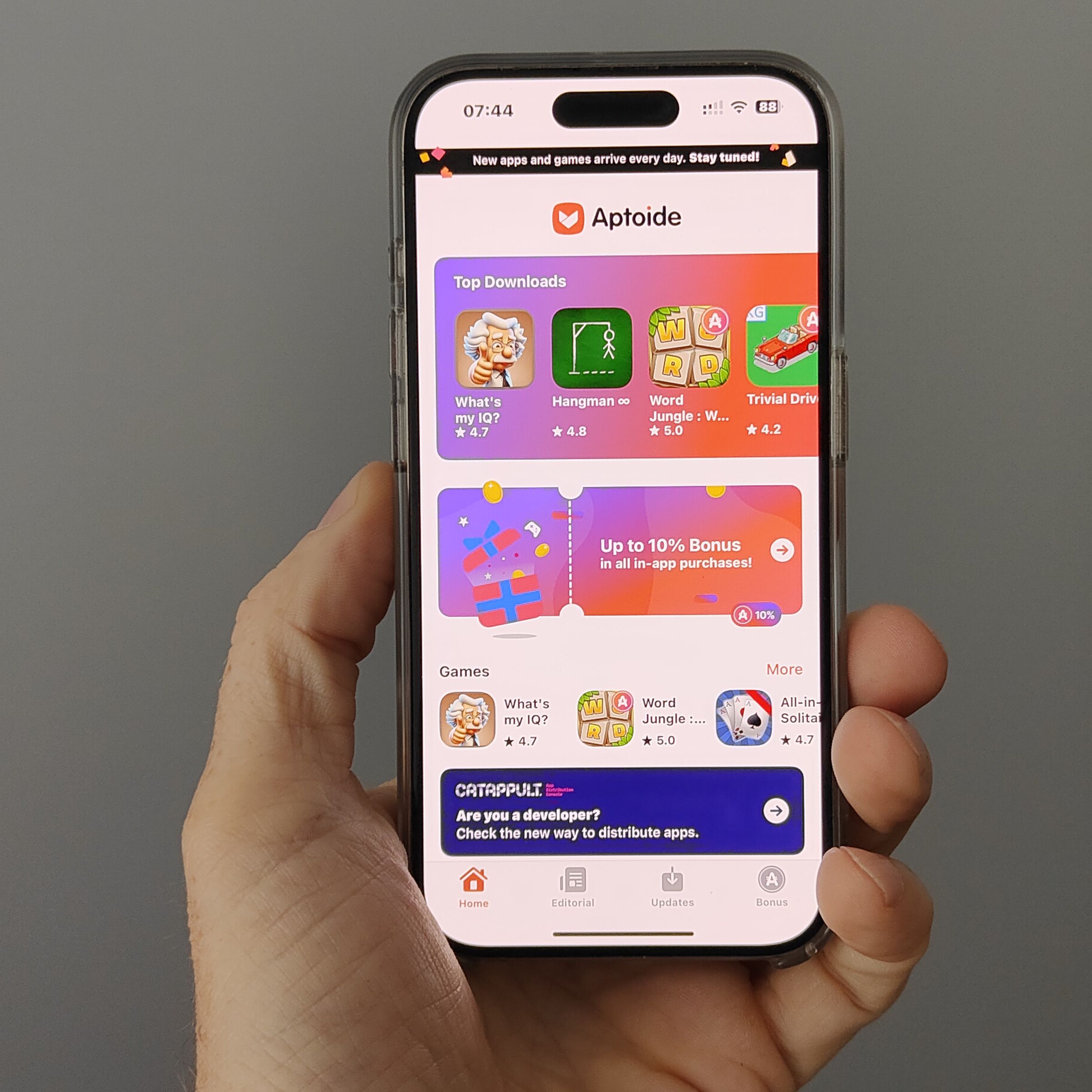 An iPhone held aloft in one hand shows the Aptoide iOS game store landing page full of colorful icons for the few games available.