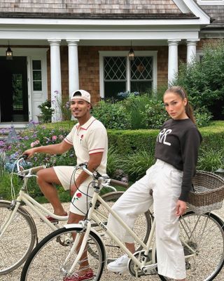 Jennifer Lopez wears cropped trousers, white sneakers, and a black sweater while sitting on a bike.