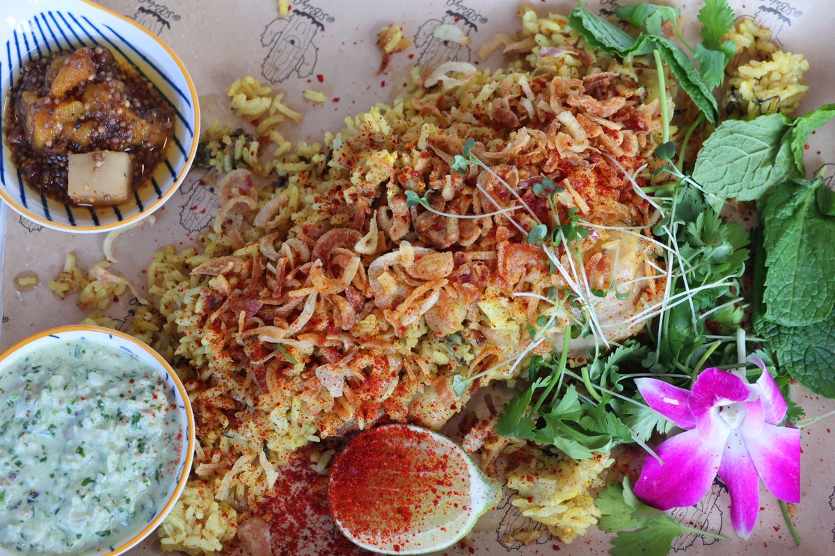 A tray of rice with chicken, bowls of sauces, and greens. 