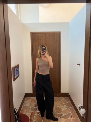 Eliza Huber wearing a one-shoulder tan top and black trousers from the Laura Harrier x Reformation collection.