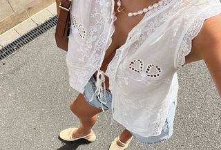 Woman in embroidered white blouse and denim shorts.