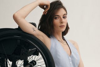 An Anthropologie model sits next to the wheel of her wheelchair posing with one arm up by her head while wearing a striped blue-and-white vest.