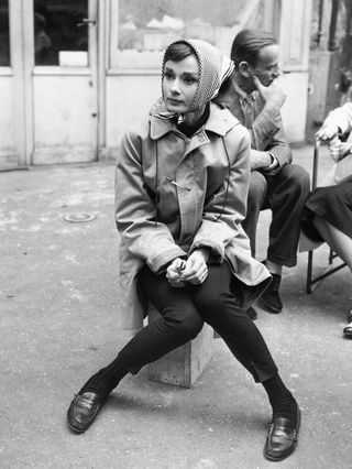 Actress Audrey Hepburn (1929–1993) sitting on a crate near the Eiffel Tower in Paris during the filming of Funny Face in 1956. Co-star Fred Astaire (1899–1987) is behind her.