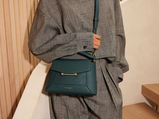 a model wears a gray outfit with a dark green crossbody bag by Strathberry