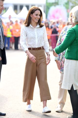 Kate Middleton wears white Superga sneakers with a white blouse and brown pants