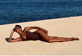 Model Jasmine Tookes wears brown one-piece swimsuit on beach.