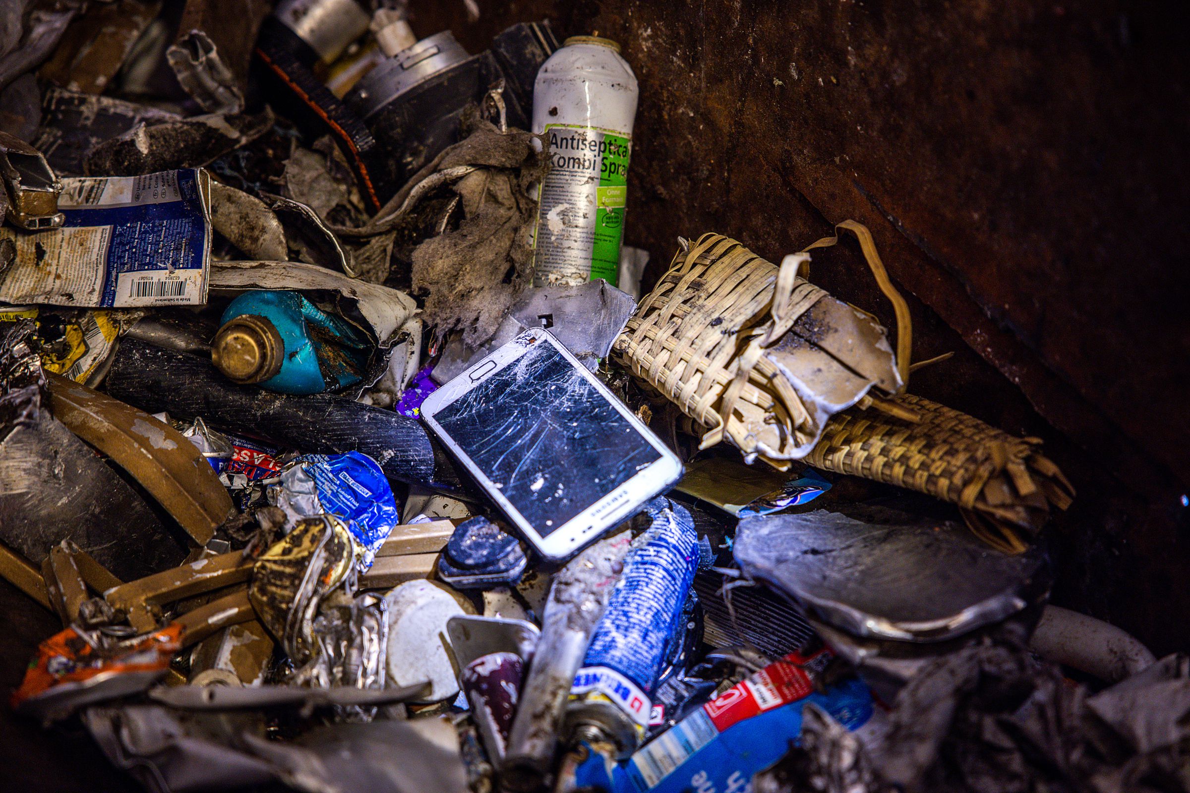 A cellphone with a cracked screen seen in a pile of trash.