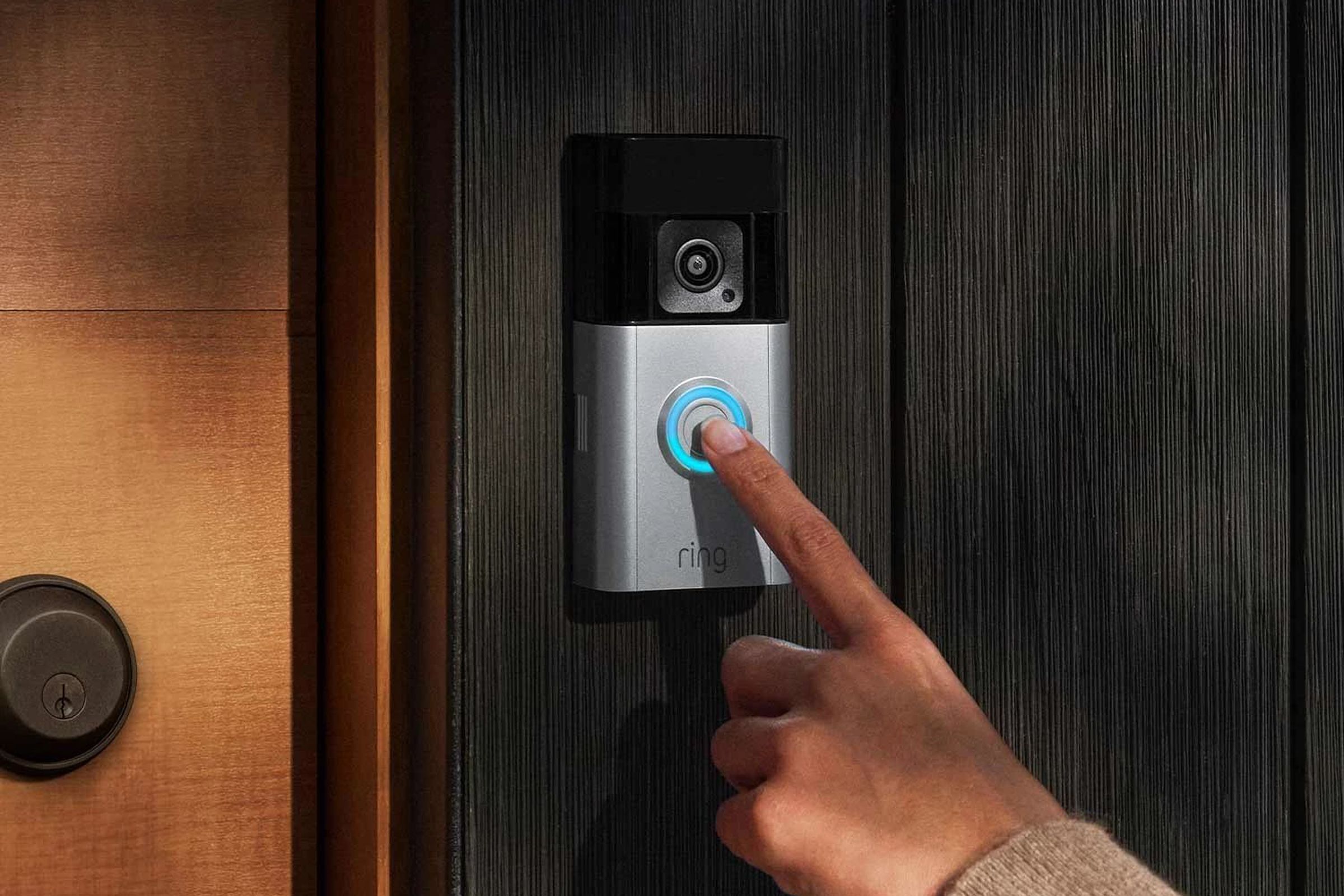 A finger pressing a video doorbell on a door frame.