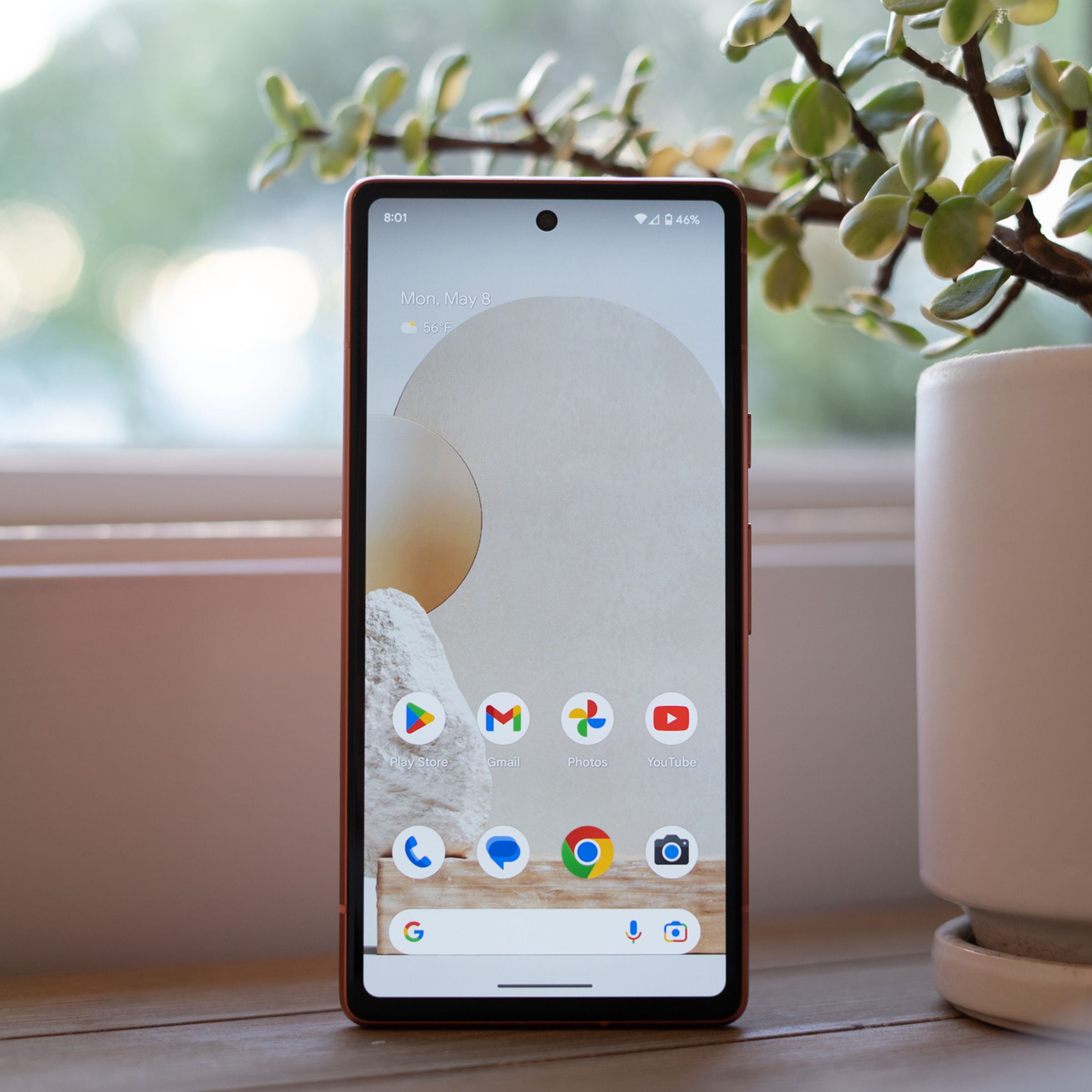 Google Pixel 7A standing upright on a table showing home screen.