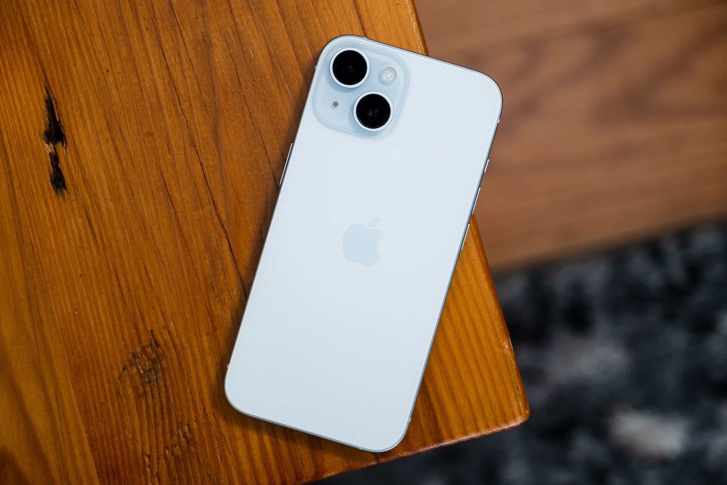 iPhone 15 on a wooden table showing rear panel in light blue color.