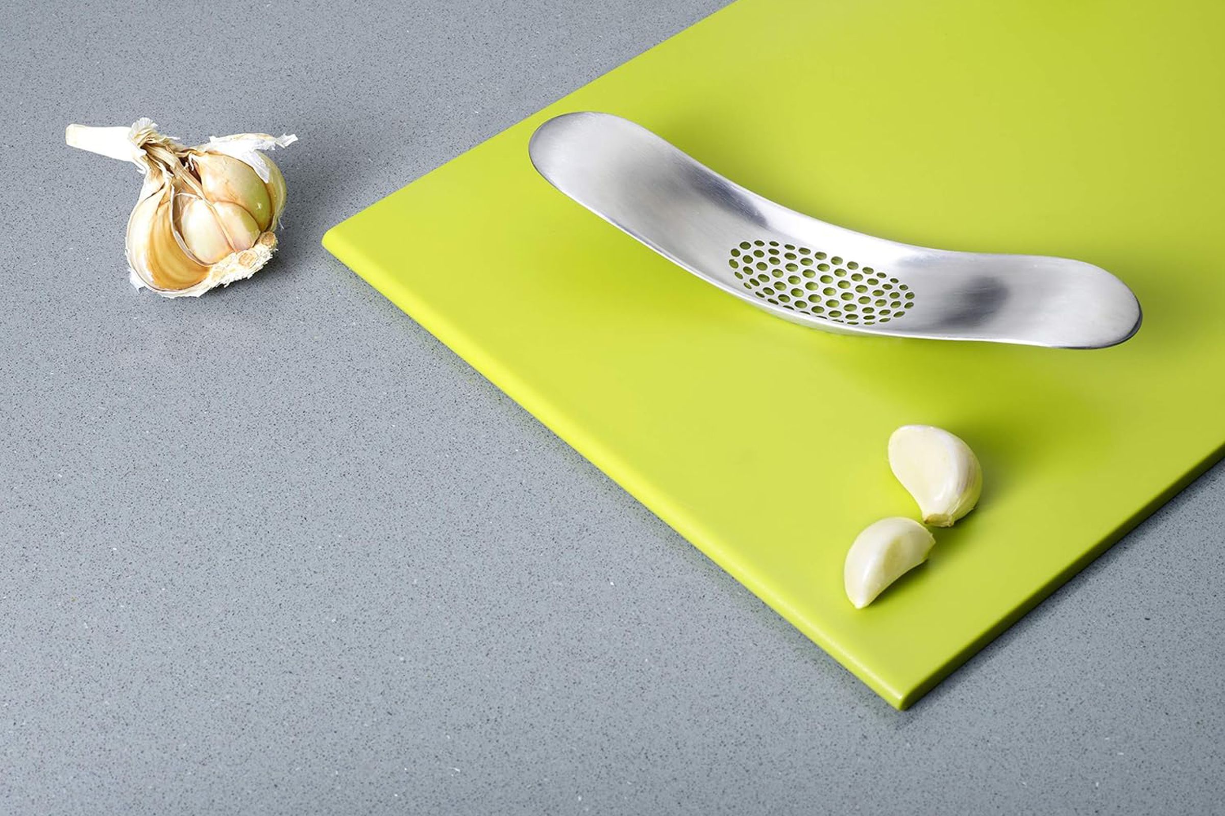 Silver garlic rocker on cutting board with garlic next to it.