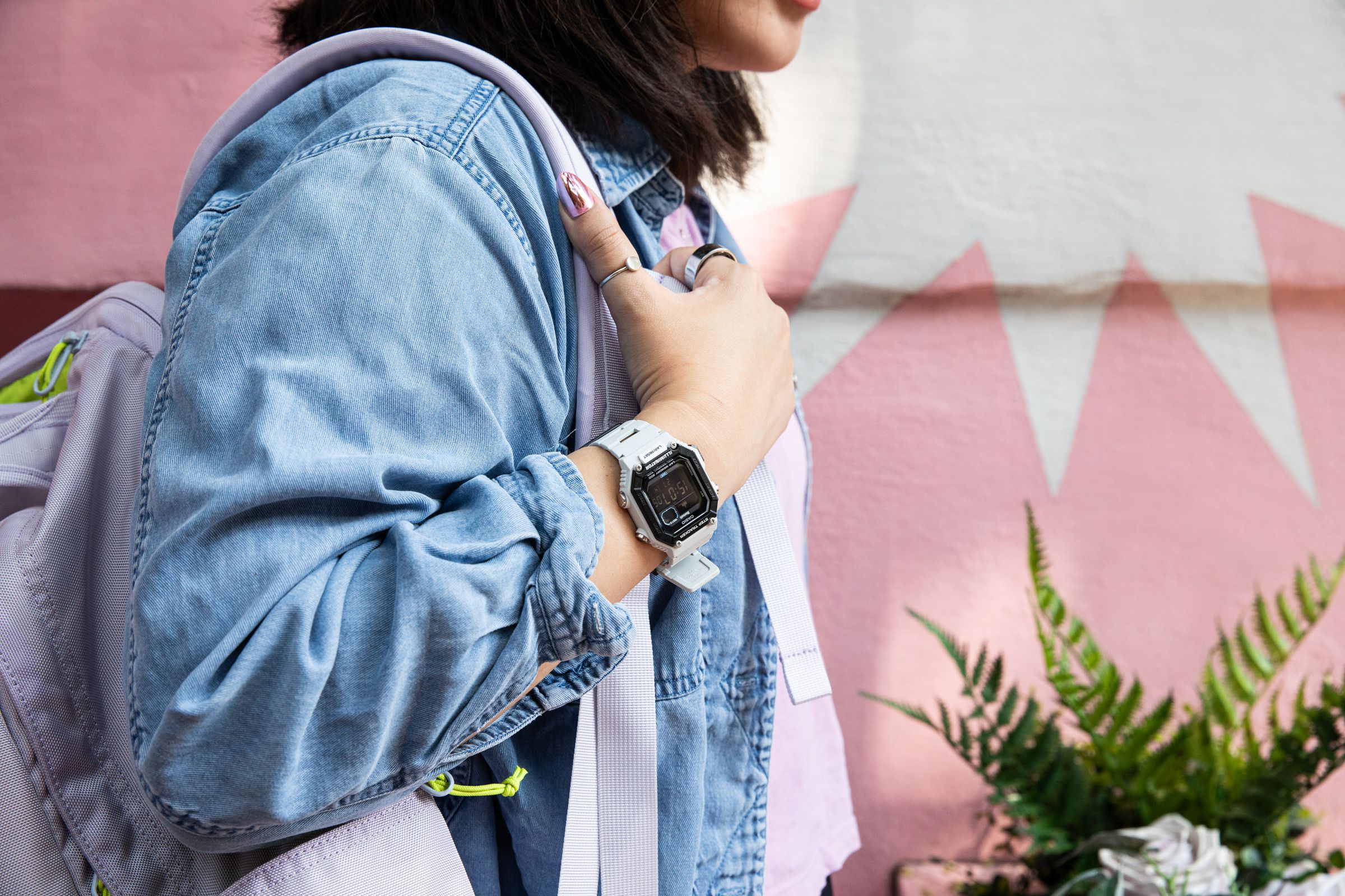 Wide shot of person wearing Casio WS-B1000 while holding a backpack in front of a pastel background