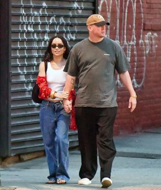 A photo of Zoë Kravitz wearing a white tank top, red shirt, low-rise jeans, and The Row blue jelly flip flops arm in arm with Channing Tatum.