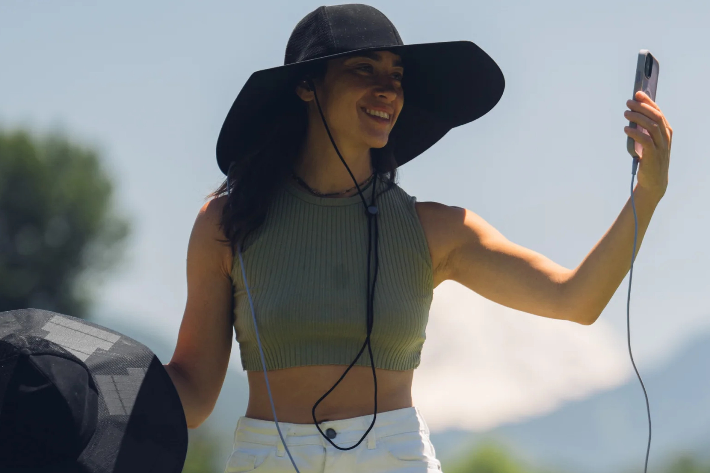 A picture of a smiling woman wearing the Power Hat and looking at her smartphone, which is plugged into the hat.