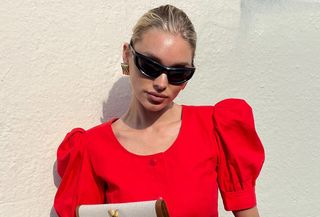 Elsa Hosk wears black sporty sunglasses, gold earrings, a red peplum top, and a Saint Laurent envelope clutch.