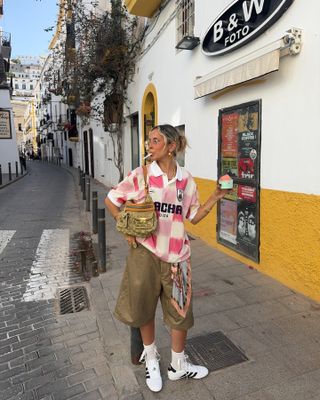 Sofia Coehlo wears Adidas Taekwondo sneakers in white with khaki Bermuda shorts, a sports jersey, and a shoulder bag.