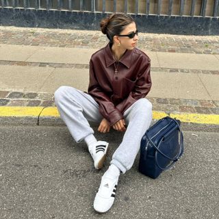 Daniela wearing Adidas Taekwondo white sneakers with gray sweatpants, a burgundy leather jacket, and a navy handbag.