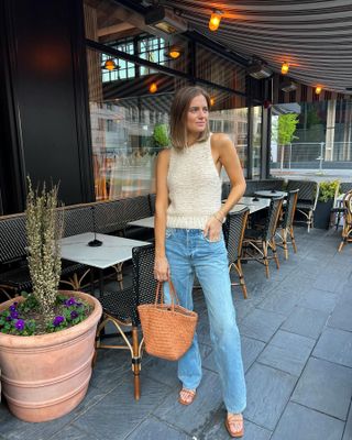 Bethany Holmes wears light-wash jeans, tan sandals, a tan straw bag, and a knit tank top.