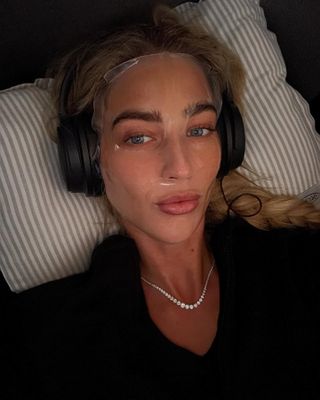 a selfie of Emili Sindlev wearing a sheet face mask and headphones on a flight