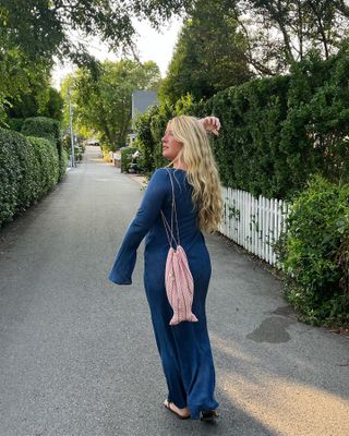 Influencer Martine Lavelle walking in Cape Cod wearing a long-sleeve blue Realisation dress, a fish-shaped bag, and flat sandals.