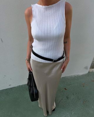 Hanna Johansson wears a white tank top, a black belt, a gray silk maxi skirt, and a black Prada bag.