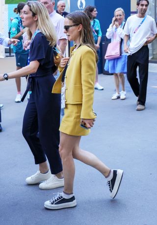 Natalie Portman wears black and white platform sneakers with a yellow skirt and matching jacket.