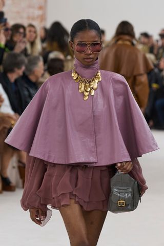 Woman in cape, sunglasses, and gold necklace.